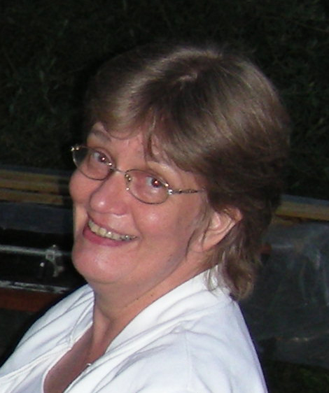 A white woman with short hair, glasses, and a white shirt smiles.